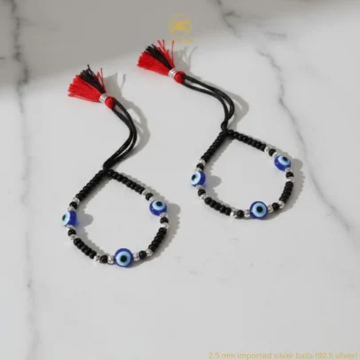 Product Description Triple the Guardian Energy, Unmatched Artisan Shine. Give your little one the ultimate shield of safety and style with the KJJ Elite Triple Evil Eye Nazariya. This premium set features three vibrant blue evil eye charms per bracelet, strategically placed to offer maximum spiritual protection from every angle. These sacred charms are beautifully paired with 2.5mm imported chevron-textured silver balls, which feature intricate "V" patterns designed to catch and reflect light with every tiny movement. Handcrafted with certified 92.5 Sterling Silver, these bracelets are meticulously hand-strung on a soft, durable black cord with polished black beads to ward off negative energy. Designed specifically for sensitive infant skin, this set ensures your baby remains shielded with high-quality materials and a touch of modern, textured luxury. Key Highlights: Triple Evil Eye Protection: Features three distinct blue evil eye charms on each bracelet for enhanced spiritual safeguarding and a bold, festive look. Chevron-Textured 2.5mm Beads: Includes premium imported silver balls with an artistic faceted texture that provides superior brilliance compared to standard smooth beads. Certified 92.5 Sterling Purity: Every silver component is made from guaranteed high-purity silver, ensuring it is hypoallergenic, lead-free, and safe for newborns. Signature Tassel Finish: Finished with our iconic red and black artisan tassel, adding a traditional touch while providing a secure, adjustable fit for growing wrists. A Meaningful Blessing: An ideal choice for "Namkaran" (naming ceremonies), first birthdays, or as a protective homecoming gift from loved ones. Product Specifications: Brand: Kanhaji Jewels (KJJ) Material: 92.5 Sterling Silver & High-Grade Protective Beads Silver Ball Texture: 2.5mm Chevron-Cut (Imported) Category: Infant Protection Jewelry / Nazariya Quantity: 1 Pair (Set of 2)