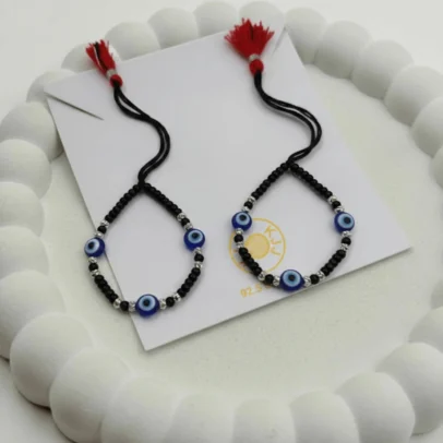 Product Description Triple the Guardian Energy, Unmatched Artisan Shine. Give your little one the ultimate shield of safety and style with the KJJ Elite Triple Evil Eye Nazariya. This premium set features three vibrant blue evil eye charms per bracelet, strategically placed to offer maximum spiritual protection from every angle. These sacred charms are beautifully paired with 2.5mm imported chevron-textured silver balls, which feature intricate "V" patterns designed to catch and reflect light with every tiny movement. Handcrafted with certified 92.5 Sterling Silver, these bracelets are meticulously hand-strung on a soft, durable black cord with polished black beads to ward off negative energy. Designed specifically for sensitive infant skin, this set ensures your baby remains shielded with high-quality materials and a touch of modern, textured luxury. Key Highlights: Triple Evil Eye Protection: Features three distinct blue evil eye charms on each bracelet for enhanced spiritual safeguarding and a bold, festive look. Chevron-Textured 2.5mm Beads: Includes premium imported silver balls with an artistic faceted texture that provides superior brilliance compared to standard smooth beads. Certified 92.5 Sterling Purity: Every silver component is made from guaranteed high-purity silver, ensuring it is hypoallergenic, lead-free, and safe for newborns. Signature Tassel Finish: Finished with our iconic red and black artisan tassel, adding a traditional touch while providing a secure, adjustable fit for growing wrists. A Meaningful Blessing: An ideal choice for "Namkaran" (naming ceremonies), first birthdays, or as a protective homecoming gift from loved ones. Product Specifications: Brand: Kanhaji Jewels (KJJ) Material: 92.5 Sterling Silver & High-Grade Protective Beads Silver Ball Texture: 2.5mm Chevron-Cut (Imported) Category: Infant Protection Jewelry / Nazariya Quantity: 1 Pair (Set of 2)