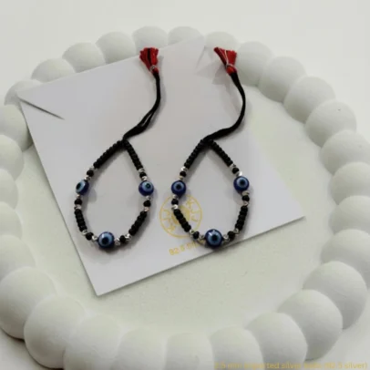 Embrace Divine Protection and Elegance for Your Little One. Keep your baby safe and stylish with our handcrafted Kanhaji Jewels (KJJ) Nazariya bracelets. Specially designed for delicate wrists, these bracelets combine traditional protection with the premium quality of 92.5 Sterling Silver. Each bracelet features imported 2.5mm pure silver balls nestled between classic black beads and vibrant blue evil eye charms. The adjustable black thread ensures a soft, comfortable fit that grows with your child, making it the perfect gift for newborns and toddlers alike. Key Features: Certified Purity: Crafted with genuine 92.5% Sterling Silver components for lasting shine and durability. Imported Silver Beads: Features premium 2.5mm silver balls that add a touch of luxury to the traditional design. Ultimate Protection: The blue evil eye charms are traditionally believed to ward off negativity and keep your little one safe. Gentle on Skin: Made with high-quality, non-irritating materials suitable for sensitive baby skin. Perfect for Gifting: An ideal choice for baby showers, naming ceremonies (Namkaran), or first birthdays. Product Specifications: Brand: Kanhaji Jewels (KJJ) Material: 92.5 Sterling Silver & High-Grade Black Thread Silver Ball Size: 2.5 mm Set Includes: 1 Pair (2 Bracelets)