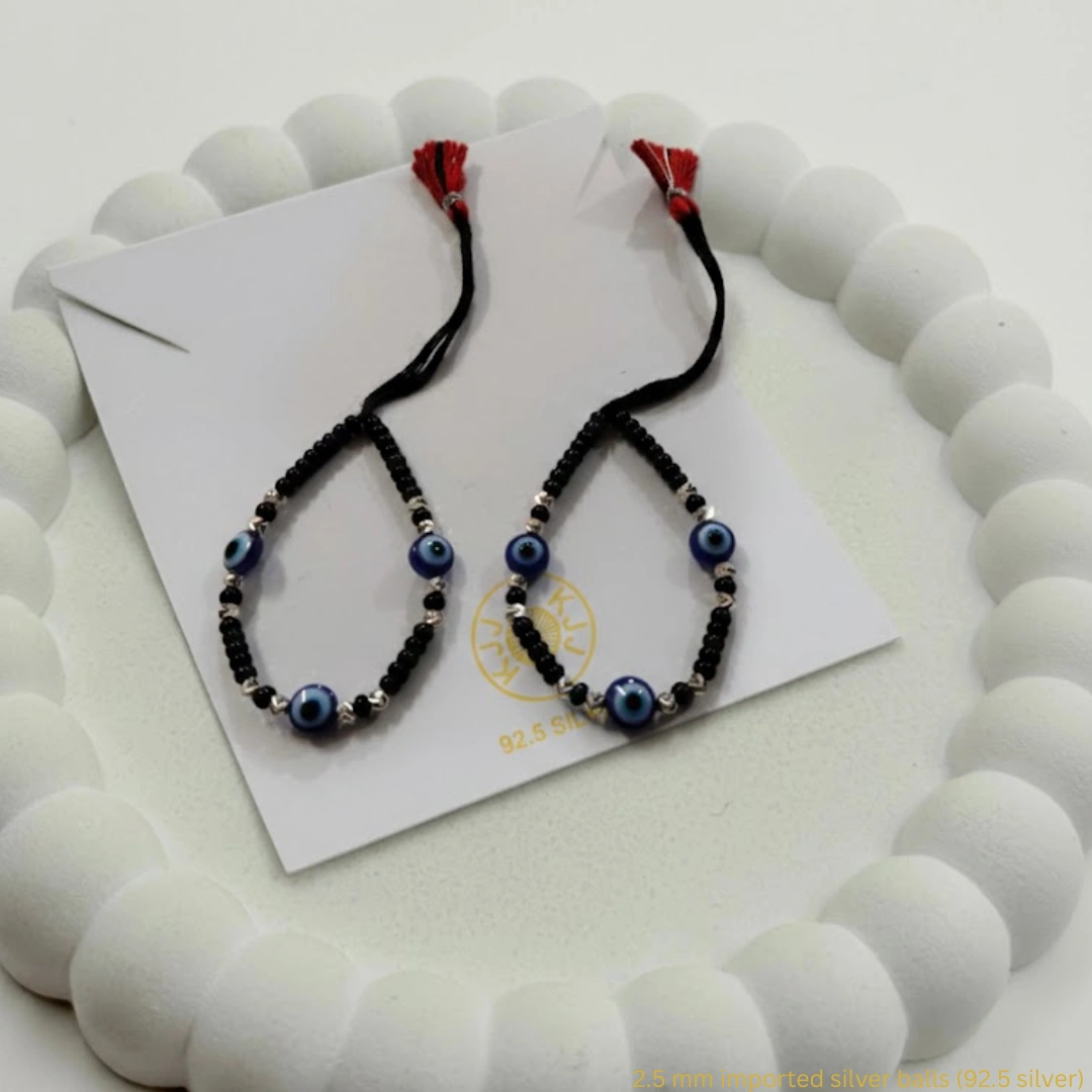 Embrace Divine Protection and Elegance for Your Little One. Keep your baby safe and stylish with our handcrafted Kanhaji Jewels (KJJ) Nazariya bracelets. Specially designed for delicate wrists, these bracelets combine traditional protection with the premium quality of 92.5 Sterling Silver. Each bracelet features imported 2.5mm pure silver balls nestled between classic black beads and vibrant blue evil eye charms. The adjustable black thread ensures a soft, comfortable fit that grows with your child, making it the perfect gift for newborns and toddlers alike. Key Features: Certified Purity: Crafted with genuine 92.5% Sterling Silver components for lasting shine and durability. Imported Silver Beads: Features premium 2.5mm silver balls that add a touch of luxury to the traditional design. Ultimate Protection: The blue evil eye charms are traditionally believed to ward off negativity and keep your little one safe. Gentle on Skin: Made with high-quality, non-irritating materials suitable for sensitive baby skin. Perfect for Gifting: An ideal choice for baby showers, naming ceremonies (Namkaran), or first birthdays. Product Specifications: Brand: Kanhaji Jewels (KJJ) Material: 92.5 Sterling Silver & High-Grade Black Thread Silver Ball Size: 2.5 mm Set Includes: 1 Pair (2 Bracelets)