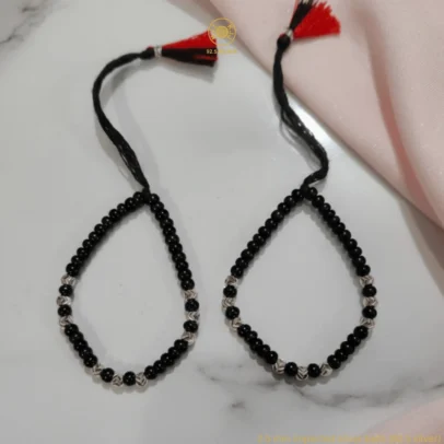 Sophisticated Shine Meets Timeless Protection. Elevate your baby’s daily wear with the KJJ Signature Baby Nazariya. This set is designed for those who appreciate fine artistic detail, featuring premium 2.5mm imported silver balls with an exquisite chevron-textured finish. The delicate "V" patterns engraved on the silver beads create a multi-faceted sparkle, offering a luxurious twist on the traditional protective "Kala Dhaga". Handcrafted with certified 92.5 Sterling Silver, these bracelets are meticulously hand-strung with high-quality black beads to provide a powerful shield against the "evil eye". The combination of textured silver and smooth black beads creates a sophisticated aesthetic that is perfect for both daily wear and special family milestones. Key Highlights: Exclusive Chevron Texture: Features precision-crafted 2.5mm silver balls with a unique chevron (V-cut) pattern for a high-end, artistic look. Certified 92.5 Sterling Purity: Every silver bead is made of guaranteed high-purity silver, ensuring it is skin-friendly, durable, and safe for infants. Traditional Nazar Protection: Designed to carry on the sacred tradition of warding off negative energy with premium craftsmanship. Adjustable & Comfortable: Fitted on a soft, durable black thread with a signature red and black tassel, allowing for a perfect, adjustable fit as your baby grows. A Gift of Love and Luxury: An exceptional choice for naming ceremonies, first birthdays, or a meaningful homecoming gift for a newborn. Product Specifications: Brand: Kanhaji Jewels (KJJ) Material: 92.5 Sterling Silver & Premium Black Beads Silver Ball Texture: 2.5mm Chevron-Cut (Imported) Set Includes: 1 Pair (2 Bracelets) Quantity: 2 Bracelets