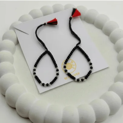 Sophisticated Shine Meets Timeless Protection. Elevate your baby’s daily wear with the KJJ Signature Baby Nazariya. This set is designed for those who appreciate fine artistic detail, featuring premium 2.5mm imported silver balls with an exquisite chevron-textured finish. The delicate "V" patterns engraved on the silver beads create a multi-faceted sparkle, offering a luxurious twist on the traditional protective "Kala Dhaga". Handcrafted with certified 92.5 Sterling Silver, these bracelets are meticulously hand-strung with high-quality black beads to provide a powerful shield against the "evil eye". The combination of textured silver and smooth black beads creates a sophisticated aesthetic that is perfect for both daily wear and special family milestones. Key Highlights: Exclusive Chevron Texture: Features precision-crafted 2.5mm silver balls with a unique chevron (V-cut) pattern for a high-end, artistic look. Certified 92.5 Sterling Purity: Every silver bead is made of guaranteed high-purity silver, ensuring it is skin-friendly, durable, and safe for infants. Traditional Nazar Protection: Designed to carry on the sacred tradition of warding off negative energy with premium craftsmanship. Adjustable & Comfortable: Fitted on a soft, durable black thread with a signature red and black tassel, allowing for a perfect, adjustable fit as your baby grows. A Gift of Love and Luxury: An exceptional choice for naming ceremonies, first birthdays, or a meaningful homecoming gift for a newborn. Product Specifications: Brand: Kanhaji Jewels (KJJ) Material: 92.5 Sterling Silver & Premium Black Beads Silver Ball Texture: 2.5mm Chevron-Cut (Imported) Set Includes: 1 Pair (2 Bracelets) Quantity: 2 Bracelets