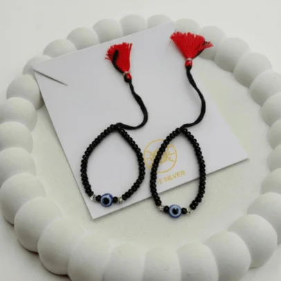 Divine Protection Wrapped in Artistic Elegance. Gift your little one the ultimate symbol of safety and style with the KJJ Signature Baby Nazariya. This premium set features a striking central blue evil eye charm, beautifully framed by 2.5mm chevron-textured imported silver balls. The intricate "V" patterns on the silver beads catch the light with every tiny movement, providing a sophisticated and luxurious sparkle that honors the sacred "Kala Dhaga" tradition. Handcrafted with certified 92.5 Sterling Silver, these bracelets are meticulously hand-strung with high-quality black beads on a soft, durable cord. Designed to be as gentle as a mother’s touch, this set ensures your baby remains shielded from negative energy while looking their absolute best. Key Highlights: Exclusive Chevron Texture: Features precision-crafted 2.5mm silver balls with an imported chevron-engraved finish for a high-end, multi-faceted shine. Certified 92.5 Purity: Every silver bead and accent is made from guaranteed high-purity sterling silver, making it hypoallergenic and safe for sensitive infant skin. Central Evil Eye Protection: Adorned with a vibrant blue evil eye charm at the center, traditionally used to ward off negativity and bring good fortune. Adjustable & Comfortable: Fitted on a soft black thread with a signature red and black tassel, allowing for a perfect, adjustable fit as your baby grows. A Meaningful Heirloom Gift: The perfect choice for Baby Showers, Naming Ceremonies, or as a protective first accessory for newborns. Product Specifications: Brand: Kanhaji Jewels (KJJ) Material: 92.5 Sterling Silver & High-Grade Black Protective Beads Silver Ball Size: 2.5mm (Imported Chevron-Cut) Category: Infant Protection Jewelry / Nazariya Quantity: 1 Pair (Set of 2)