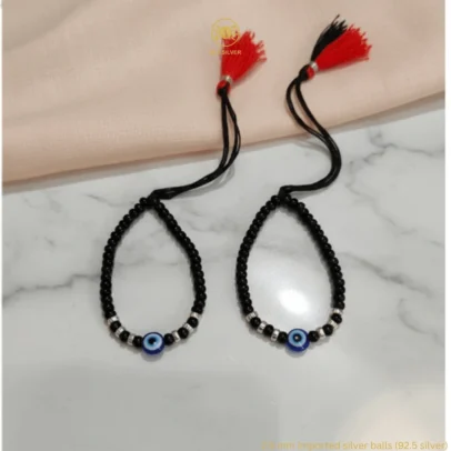 Sophisticated Texture for Sacred Protection. Elevate your baby's daily wardrobe with the KJJ Elite Baby Nazariya, where artistic detail meets traditional shielding. This premium set features a striking central blue evil eye charm flanked by unique 2.5mm imported silver balls with a corrugated (ridged) texture. The fine vertical lines on these silver beads catch the light with every tiny movement, providing a rich, multi-dimensional sparkle that sets this piece apart from standard smooth-bead designs. Handcrafted with certified 92.5 Sterling Silver, these bracelets are meticulously hand-strung on a soft, durable black cord with polished black beads to ward off negative energy. Designed to be as gentle as it is beautiful, this set ensures your little one stays protected with the highest quality materials and a touch of modern luxury. Key Highlights: Unique Corrugated Silver Texture: Features premium 2.5mm imported silver balls with a distinctive ridged pattern for an upscale and light-catching finish. Certified 92.5 Sterling Purity: Every silver bead is made from guaranteed high-purity silver, ensuring a hypoallergenic and long-lasting shine that is safe for infants. Sacred Evil Eye Protection: Adorned with a vibrant blue evil eye charm at the center, traditionally used to shield children from the "evil eye" and bring good fortune. Adjustable Artisan Cord: Fitted on a soft black thread with our signature red and black tassel, providing a secure and custom fit as your baby grows. A Gift of Devotion and Quality: The perfect choice for "Namkaran" ceremonies, first birthdays, or as a meaningful homecoming blessing for a newborn. Product Specifications: Brand: Kanhaji Jewels (KJJ) Material: 92.5 Sterling Silver & High-Grade Protective Beads Silver Ball Texture: 2.5mm Corrugated / Ridged (Imported) Category: Infant Protection Jewelry / Nazariya Quantity: 1 Pair (Set of 2)