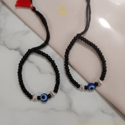 Sophisticated Texture for Sacred Protection. Elevate your baby's daily wardrobe with the KJJ Elite Baby Nazariya, where artistic detail meets traditional shielding. This premium set features a striking central blue evil eye charm flanked by unique 2.5mm imported silver balls with a corrugated (ridged) texture. The fine vertical lines on these silver beads catch the light with every tiny movement, providing a rich, multi-dimensional sparkle that sets this piece apart from standard smooth-bead designs. Handcrafted with certified 92.5 Sterling Silver, these bracelets are meticulously hand-strung on a soft, durable black cord with polished black beads to ward off negative energy. Designed to be as gentle as it is beautiful, this set ensures your little one stays protected with the highest quality materials and a touch of modern luxury. Key Highlights: Unique Corrugated Silver Texture: Features premium 2.5mm imported silver balls with a distinctive ridged pattern for an upscale and light-catching finish. Certified 92.5 Sterling Purity: Every silver bead is made from guaranteed high-purity silver, ensuring a hypoallergenic and long-lasting shine that is safe for infants. Sacred Evil Eye Protection: Adorned with a vibrant blue evil eye charm at the center, traditionally used to shield children from the "evil eye" and bring good fortune. Adjustable Artisan Cord: Fitted on a soft black thread with our signature red and black tassel, providing a secure and custom fit as your baby grows. A Gift of Devotion and Quality: The perfect choice for "Namkaran" ceremonies, first birthdays, or as a meaningful homecoming blessing for a newborn. Product Specifications: Brand: Kanhaji Jewels (KJJ) Material: 92.5 Sterling Silver & High-Grade Protective Beads Silver Ball Texture: 2.5mm Corrugated / Ridged (Imported) Category: Infant Protection Jewelry / Nazariya Quantity: 1 Pair (Set of 2)
