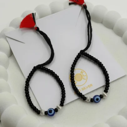 Sophisticated Texture for Sacred Protection. Elevate your baby's daily wardrobe with the KJJ Elite Baby Nazariya, where artistic detail meets traditional shielding. This premium set features a striking central blue evil eye charm flanked by unique 2.5mm imported silver balls with a corrugated (ridged) texture. The fine vertical lines on these silver beads catch the light with every tiny movement, providing a rich, multi-dimensional sparkle that sets this piece apart from standard smooth-bead designs. Handcrafted with certified 92.5 Sterling Silver, these bracelets are meticulously hand-strung on a soft, durable black cord with polished black beads to ward off negative energy. Designed to be as gentle as it is beautiful, this set ensures your little one stays protected with the highest quality materials and a touch of modern luxury. Key Highlights: Unique Corrugated Silver Texture: Features premium 2.5mm imported silver balls with a distinctive ridged pattern for an upscale and light-catching finish. Certified 92.5 Sterling Purity: Every silver bead is made from guaranteed high-purity silver, ensuring a hypoallergenic and long-lasting shine that is safe for infants. Sacred Evil Eye Protection: Adorned with a vibrant blue evil eye charm at the center, traditionally used to shield children from the "evil eye" and bring good fortune. Adjustable Artisan Cord: Fitted on a soft black thread with our signature red and black tassel, providing a secure and custom fit as your baby grows. A Gift of Devotion and Quality: The perfect choice for "Namkaran" ceremonies, first birthdays, or as a meaningful homecoming blessing for a newborn. Product Specifications: Brand: Kanhaji Jewels (KJJ) Material: 92.5 Sterling Silver & High-Grade Protective Beads Silver Ball Texture: 2.5mm Corrugated / Ridged (Imported) Category: Infant Protection Jewelry / Nazariya Quantity: 1 Pair (Set of 2)