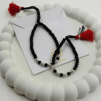 Celestial Brilliance for Your Little Star. Give your baby a touch of high-end sparkle with the KJJ Radiant Baby Nazariya. This exquisite set features premium 2.5mm imported silver balls with a unique star-cut (diamond-cut) texture, designed to catch and reflect light from every angle. These faceted silver beads provide a brilliant, jewel-like shine that elevates the traditional protective "Kala Dhaga" into a sophisticated piece of fine infant jewelry. Handcrafted with certified 92.5 Sterling Silver, these bracelets are meticulously hand-strung on a soft, durable black cord with polished black beads to ward off negative energy. Designed specifically for delicate infant skin, this set ensures your baby stays protected with the highest quality materials and a stunning, modern radiance. Key Highlights: Unique Star-Cut Texture: Features premium 2.5mm imported silver balls with a precision-faceted surface that offers significantly more sparkle than standard smooth beads. 92.5% Sterling Purity: Every silver component is guaranteed certified high-purity silver, ensuring it is hypoallergenic, lead-free, and safe for newborns. Sacred Nazar Protection: Combines the spiritual significance of black protective beads with pure silver to shield your child from the "evil eye". Artisan Tassel Finish: Finished with our signature red and black tassel, adding a traditional touch while providing a secure, adjustable fit as your baby grows. A Gift of Exceptional Quality: An ideal and luxurious choice for "Namkaran" (naming ceremonies), first birthdays, or a protective homecoming gift. Product Specifications: Brand: Kanhaji Jewels (KJJ) Material: 92.5 Sterling Silver & High-Grade Protective Beads Silver Ball Texture: 2.5mm Star-Cut / Diamond-Cut (Imported) Category: Infant Protection Jewelry / Nazariya Quantity: 1 Pair (Set of 2)