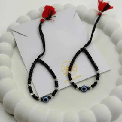 Artisan Sparkle for Sacred Security. Give your little one the ultimate symbol of safety and style with the KJJ Elite Baby Nazariya. This premium protective set features a vibrant central blue evil eye charm, beautifully accented by 2.5mm chevron-textured imported silver balls. The delicate "V" patterns engraved on the silver beads catch the light brilliantly, offering a sophisticated and modern twist on the traditional "Kala Dhaga". Handcrafted with certified 92.5 Sterling Silver, these bracelets are meticulously hand-strung on a soft, durable black cord with polished black beads to ward off negative energy. Designed specifically for sensitive infant skin, this set ensures your baby remains protected with high-quality materials and a touch of luxury. Key Highlights: 92.5 Sterling Silver Purity: Every silver bead and accent is made from certified high-purity silver, making it safe, hypoallergenic, and long-lasting for newborns. 2.5mm Chevron-Textured Beads: Features premium imported silver balls with an artistic faceted texture that provides more brilliance than standard smooth beads. Sacred Evil Eye Protection: Adorned with a striking blue evil eye charm at the center, traditionally used to shield children from negativity and bring peace. Adjustable Artisan Cord: Fitted on a soft black thread with a signature red and black tassel, providing a traditional look and a secure, adjustable fit as your baby grows. A Meaningful Blessing: An ideal choice for "Namkaran" (naming ceremonies), first birthdays, or a protective first accessory for a new arrival. Product Specifications: Brand: Kanhaji Jewels (KJJ) Material: 92.5 Sterling Silver & High-Grade Protective Beads Silver Ball Texture: 2.5mm Chevron-Cut (Imported) Category: Infant Protection Jewelry / Nazariya Quantity: 1 Pair (Set of 2)