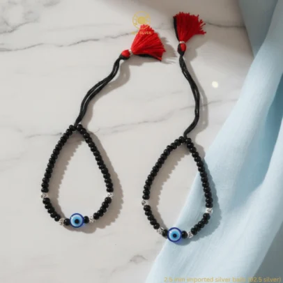 Product Description Divine Protection with Artisan Sparkle. Surround your baby with a shield of love and ancient tradition with the KJJ Elite Baby Nazariya. This premium protective set features a vibrant central blue evil eye charm, beautifully accented by 2.5mm imported silver balls with an exquisite chevron (V-cut) texture. The multi-faceted patterns on the silver beads are designed to catch and reflect light, providing a sophisticated radiance that honors the sacred "Kala Dhaga" tradition. Handcrafted with certified 92.5 Sterling Silver, these bracelets are hand-strung on a soft, durable black cord with polished black beads to ward off negative energy. Designed specifically for sensitive infant skin, this set ensures your little one remains protected with the highest quality materials and a touch of modern, textured luxury. Key Highlights: Exclusive Chevron Texture: Features premium 2.5mm imported silver balls with an engraved chevron finish for a multi-faceted and high-end shine. Certified 92.5 Sterling Purity: Every silver bead and accent is made from guaranteed high-purity silver, ensuring it is hypoallergenic and safe for newborns. Sacred Evil Eye Protection: Adorned with a striking blue evil eye charm at the center, traditionally used to shield children from negativity and bring peace. Signature Tassel Finish: Finished with our iconic red and black artisan tassel, adding a traditional touch while providing a secure, adjustable fit for growing wrists. A Meaningful Blessing: An ideal choice for "Namkaran" (naming ceremonies), first birthdays, or as a protective homecoming gift. Product Specifications: Brand: Kanhaji Jewels (KJJ) Material: 92.5 Sterling Silver & High-Grade Protective Beads Silver Ball Texture: 2.5mm Chevron-Cut (Imported) Category: Infant Protection Jewelry / Nazariya Quantity: 1 Pair (Set of 2)