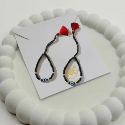 Product Description Divine Protection with Artisan Sparkle. Surround your baby with a shield of love and ancient tradition with the KJJ Elite Baby Nazariya. This premium protective set features a vibrant central blue evil eye charm, beautifully accented by 2.5mm imported silver balls with an exquisite chevron (V-cut) texture. The multi-faceted patterns on the silver beads are designed to catch and reflect light, providing a sophisticated radiance that honors the sacred "Kala Dhaga" tradition. Handcrafted with certified 92.5 Sterling Silver, these bracelets are hand-strung on a soft, durable black cord with polished black beads to ward off negative energy. Designed specifically for sensitive infant skin, this set ensures your little one remains protected with the highest quality materials and a touch of modern, textured luxury. Key Highlights: Exclusive Chevron Texture: Features premium 2.5mm imported silver balls with an engraved chevron finish for a multi-faceted and high-end shine. Certified 92.5 Sterling Purity: Every silver bead and accent is made from guaranteed high-purity silver, ensuring it is hypoallergenic and safe for newborns. Sacred Evil Eye Protection: Adorned with a striking blue evil eye charm at the center, traditionally used to shield children from negativity and bring peace. Signature Tassel Finish: Finished with our iconic red and black artisan tassel, adding a traditional touch while providing a secure, adjustable fit for growing wrists. A Meaningful Blessing: An ideal choice for "Namkaran" (naming ceremonies), first birthdays, or as a protective homecoming gift. Product Specifications: Brand: Kanhaji Jewels (KJJ) Material: 92.5 Sterling Silver & High-Grade Protective Beads Silver Ball Texture: 2.5mm Chevron-Cut (Imported) Category: Infant Protection Jewelry / Nazariya Quantity: 1 Pair (Set of 2)